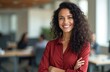 © miss irine - Young hispanic woman smiles confidently in office. She wears red shirt arms crossed. Pro person at work. Modern business environment. Copy space available.