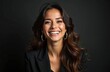 © Vadym - Brunette woman with long wavy hair smiles widely in studio. She wears a black blazer and large hoop earrings, looking confident and happy. Her makeup is natural and radiant.