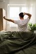 © milanmarkovic78 - Man Stretches and Wakes up in Bedroom During Morning in a Bright and Cozy Room With Plants