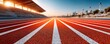 © Georgii - Macro view of a red running track with lanes stretching toward a stadium at sunrise