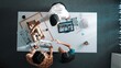 © InfiniteFlow - Top down view of civil architect looking at project plan while present to investor at meeting table. Aerial view of skilled designer explain about construction to business people listen. Alimentation.