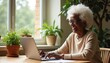 © Pete - Elderly Black woman smiles while typing on laptop computer. She looks happy during online therapy session or virtual meeting at home with plants visible.
