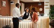 © DC Studio - Friendly asian receptionist offering room key to happy guests after check in process is finalized. Busy exhausted hotel manager ensuring booking paperwork details are correct