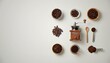 © dang - Top-down view of coffee beans, a wooden manual grinder, a wooden spoon, a measuring scoop, and a cup of black coffee arranged on a light gray surface.