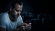© pattozher - Contemplative Connection: A man intently focuses on a smartphone, his expression reflecting deep thought and engagement in a dim, intimate setting.