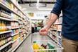 © Meow Creations - Adult man carrying a white shopping basket filled with fresh produce in a grocery store aisle