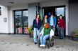 © Halfpoint - Group of teenage students supporting friend in wheelchair in front of school building.