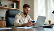 © Viktor - Bearded man pays online using credit card and laptop at desk. Person works in office with computer and card. Manager completes purchase or transaction.