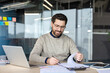 © Liubomir - Businessman working with paperwork and financial data, reviewing documents on his desk with a laptop and calculator, demonstrating focus and productivity in a contemporary workspace