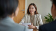 © bephoto - 明るいオフィスで書類を手に相談者と面談する日本人女性、安心感のある就職相談