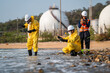 © VStudio - Environmental scientists in protective hazmat suits collecting water samples for pollution analysis and ecological research at an industrial site.