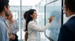 © ryker - Modern businesswoman leading presentation on touchscreen display, smiling and explaining charts to diverse team while pointing at data and graphs in bright office meeting room