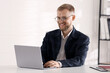 © New Africa - Smiling businessman in suit and glasses working on laptop at white table in office