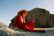 © Berena Alvarez/Stocksy - Young man in red clothing and straw hat sitting on coastal rocks