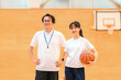 © buritora - A male teacher who is the club advisor and a female student holding a basketball are in the gymnasium.