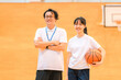 © buritora - A male teacher who is the club advisor and a female student holding a basketball are in the gymnasium.