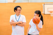 © buritora - A male teacher who is the club advisor and a female student holding a basketball are in the gymnasium.