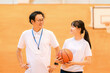© buritora - A male teacher who is the club advisor and a female student holding a basketball are in the gymnasium.