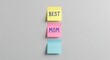 © MostZannatun - Three colorful sticky notes arranged vertically on a plain grey wall with text best mom.