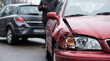 © ViskBx - Car accident on the road, damaged red car after a collision with a dark grey vehicle, driver standing in the background using a phone