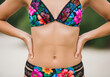 © Bijaya Kumar - A detailed close-up of a woman wearing a vibrant floral print bikini, hands on hips, standing outdoors in a tropical summer beach environment.
