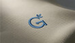 © Khadim - Embroidered letter G logo on white fabric texture, blue thread embroidery on cotton textile, elegant monogram branding mockup for fashion apparel