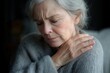 © Monika - elderly person with white hair and wrinkled hands resting a hand on the shoulder while wearing a soft gray sweater, conveying quiet reflection and gentle vulnerability