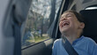 © stockcopter - Interior shot. A young boy laughs joyfully in a car seat during a sunny road trip. Scene captured from inside a moving vehicle, showcasing a casual and happy atmosphere.