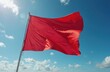 © miss irine - Bright red flag flies on metal pole against blue sky with clouds. Strong wind blows fabric creating wavy motion. Indicates beach danger, rough sea conditions.