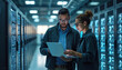 © miss irine - Two engineers examine server racks in data center. They use laptop for analysis of system performance and network status. Colleagues collaborate on tech infrastructure.