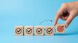 © Masque - A hand placing a wooden block with a target icon among check mark blocks for goal achievement and business success.