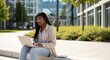 © FikriVisuals - Young student works on laptop outdoors in bright sunlight near modern corporate buildings demonstrating digital learning lifestyle