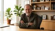 © AspctStyle - Smiling senior male executive sitting at desk in modern office. Experienced businessman, professor or consultant with arms crossed in workplace.