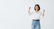 © Ariestia - Excited young Asian woman celebrates success by raising her fists in victory against a plain background.