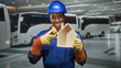 © Krakenimages.com - Man builder in hardhat points at wooden house model inside bus terminal building while smiling and wearing yellow gloves and earmuffs; pride duty.