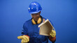 © Krakenimages.com - Black man in blue hardhat and coverall holding a wooden house model and presenting open palm while wearing yellow gloves and earmuffs in studio; pride.