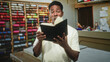 © Krakenimages.com - Man holding book touches cheek in a sewing studio surrounded by thread spools and counter; thoughtful craft pride.