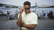 © Krakenimages.com - Man adjusts glasses with right hand showing forearm, smiling at a street cafe by the waterfront; confidence ease friendliness.
