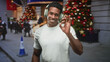 © Krakenimages.com - Man wearing headphones pointing finger on a city street near a decorated christmas tree; holiday joy celebration.