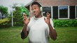 © Krakenimages.com - Black man wearing headphones snapping fingers and smiling in front of a brick building with windows and lawn; joyful groove.