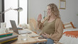 © Krakenimages.com - Pregnant woman holding belly at laptop in bedroom, smiling and cradling bump beside bed and desk while seated; contentment.