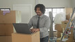 © Krakenimages.com - Man typing on laptop placed on moving box in building with packed boxes and ladder visible; productivity focus.