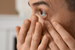 © Pixel-Shot - Young man putting in contact lenses at home, closeup