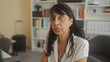 © Krakenimages.com - Woman wearing necklace closing her eyes and tilting head at a desk with suitcase and bookshelves in a building; pensive solitude.