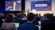 © Bertumbuh - A woman on stage giving a presentation in front of a seated audience