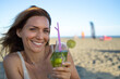 © SISMIZ - Woman smiling holding refreshing cocktail drink on beach