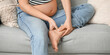 © Pixel-Shot - Young pregnant woman suffering from ankle pain on sofa at home, closeup