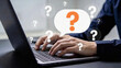 © Hendra - Person typing on a laptop with question marks floating around a speech bubble