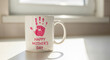 © Kristelinmind - White ceramic mug with pink handprint and text for Mothers Day. Custom gift cup for mom with child hand print. Celebration of motherhood and family love memory. Home interior setting.