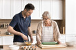 © fizkes - Older woman and young adult son cook together in modern kitchen, lead conversation on weekend at home. Millennial man helps with food preparation to middle-aged mother, smile, enjoy talk. Family time